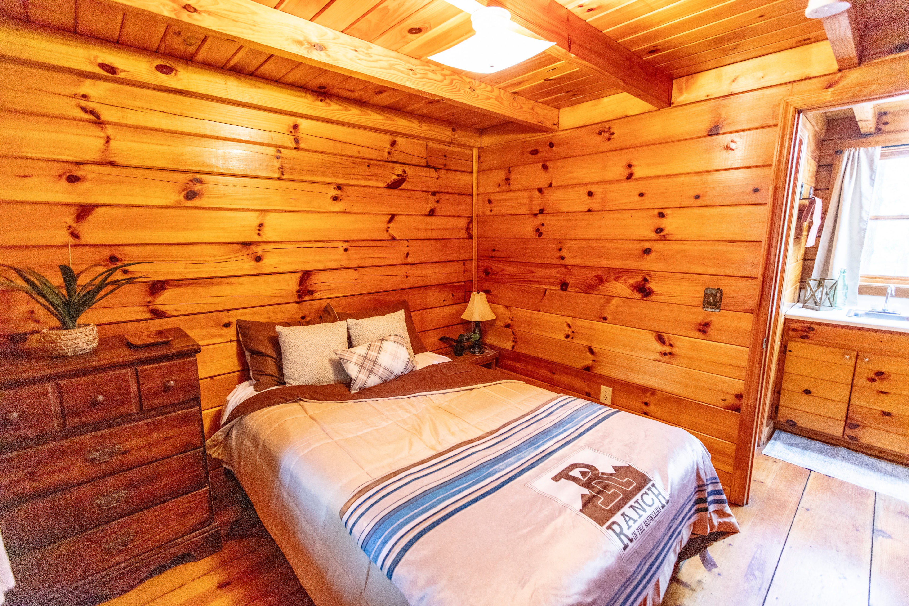 R Ranch cabin bedroom with warm wood paneling and cozy bedding